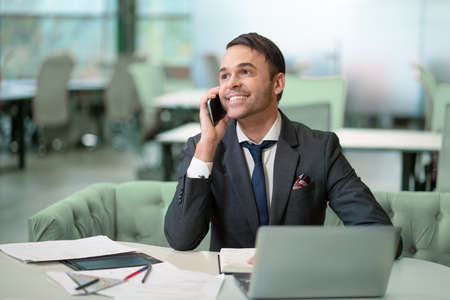 Handsome man in business suit talking on the phone working on laptop, job in progress. Cheer smiling...