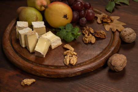 Cheese plate with fruits, grapes, nuts on a dark wooden plate and wooden table. Wine snacks set:...