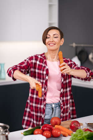Throws up washed carrots trying to juggle charming short hair housewife prepares carrot cake in the kitchen. Healthy food at home. Healthy food leaving concept. New house concept.の写真素材