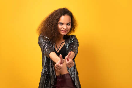 Positive beautiful ethnic girl with afro hair showing thumbs up smile looking at camera wearing...