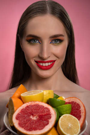 Beauty fashion model girl with beautiful make up, red lips, long healthy hair and bawl of colorful fresh cut citrus fruits in her hands. Lime, orange, lemon, grapefruit. Fashion concept.の写真素材