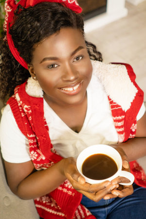 Cute Afro American Lady With a Cup of Coffee in Her Hands on Christmas Eve Waiting For a Christmas Miracle at Home. Close-up Face. High quality photoの写真素材