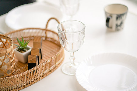 Served and Decorated White Table with Glasses, Plates and a Mug. Table Decoration with Wicker and Wooden Decor Elements. High quality photoの写真素材