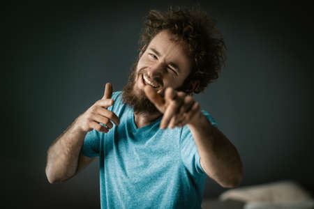 Cheerful Guy in a Blue T-shirt with Happy Eyes and a Wide Smile Points his Fingers to the Camera. Close-up Portrait. Grey Background. High quality photoの写真素材