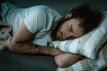 Tired Man is Fast Asleep in his Bed on a Pillow. Sleeping Man in a White T-shirt, Night Sleep, Lunchtime Dream. Break For Sleep. Close-up. High quality photoの写真素材