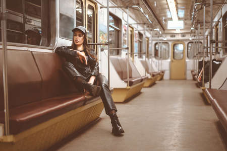 brutal woman in a leather jacket, leather pants and ankle boots sits alone in a train car. Toned picture. Close-up. High quality photoの写真素材