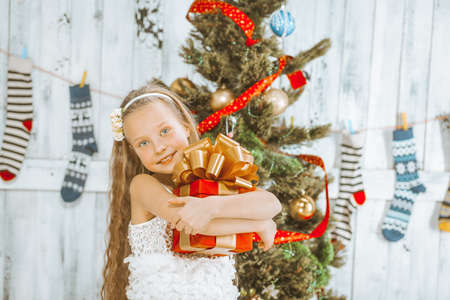 Smiling Girl Holds in her Hands a Red Square Christmas Gift Box with a Ribbon and a Lush Golden Bow. Christmas and New Year Holidays. Close-up. High quality photoの写真素材