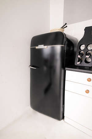 Glossy Stylish Fridge in Retro Style in White Kitchen. Black Refrigerator in Vintage Style on White Background. Close-up. High quality photoの写真素材