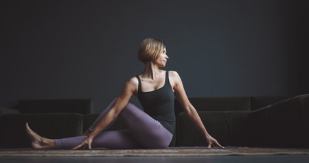 Yoga class. A beautiful, trained body. A woman makes an asana against a dark background in a city...