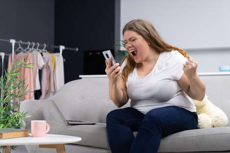 Sultry Plus Size Woman Received Positive News on the Phone and is Very Happy. Body Positive Female Model Holds a Smartphone in her Hand and Shouts Happily into the Phone. Close-up. High quality photoの写真素材