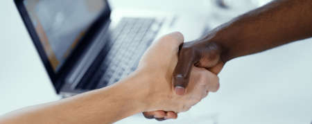 African Hand and Caucasian Hand in Handshake, International Partnership, Racial Commonwealth, Unification, Friendship. Laptop Background. Close-up. High quality photoの写真素材