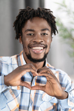 Handsome Guy in Plaid Casual Shirt Shows Heart Gesture by his Fingers. Dark Skin Male Model Makes Heart Figure by his Hands. Fell in love. Close-up. High quality photoの写真素材