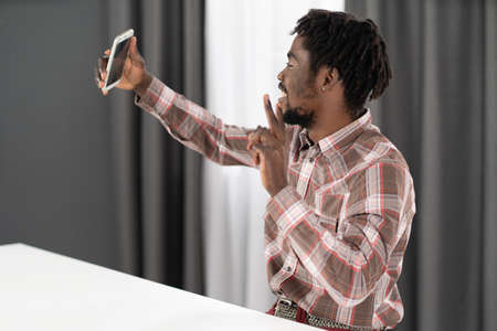 Taking selfie or having video call young african american man hold his phone in stretched hand in front. Portrait of happy man gesturing while speaking on video call. Social media concept.の写真素材