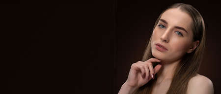 High fashion beauty girl with long healthy hair and bare shoulders looking at camera touching her chin isolated on black. Beauty concept. Hair health concept. Hair care concept.の写真素材