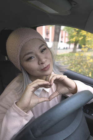 Showing love blond asian woman in the car. Mature asian woman looking at camera holding hands in...