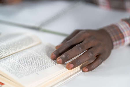 Close up african american man hand on a open book. Student preparing to the lecture at library reading books and making notes. Adduction concept.の写真素材