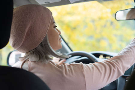 Charming blond asian woman driving car. Mature asian woman in glasses looking at the mirrow holding...