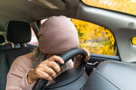 Mature woman in auto crash hit the steering wheel with head. Sleeping exhausted asian woman sleeping in the car. Blond middle aged asian woman in the car. Woman on the road. Business concept.の写真素材