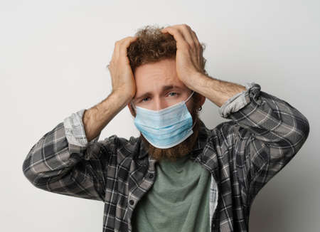 Sick young man in medical face mask feel migraine holding head. Handsome guy feel pain or headache. Exhausted young man trying to concentrate massaging his head. Health care concept.の写真素材