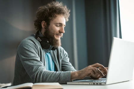 Young freelancer man working at laptop sitting at the desk at home office and making notes or...