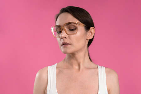 Suffering of headache or migraine young woman in sleeveless pink t-shirt holding her head with eyes shut isolated on pink background. Stressed employee woman in stripe suit. With copy space.の写真素材