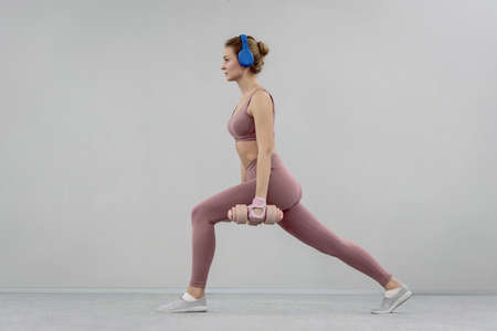 Doing step split stretch athletic young woman use heavy lifting using dumbbell at the gym. Young woman exercise using dumbbell to lose weight or burn calories. Sport concept.の写真素材