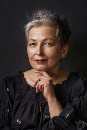 Close up gorgeous mature businesswoman with grey hair posing leaned chin on her hand isolated on black background. Graying elegant woman with short hair. Image of successful mature woman. Aged beauty.の写真素材