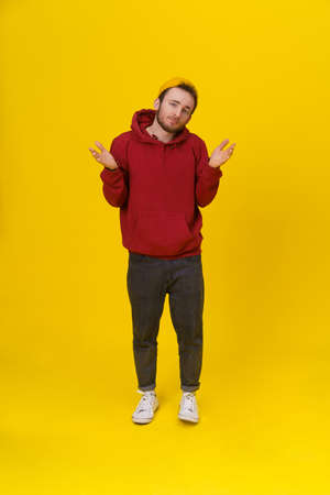 Gesturing with both hands I DONT KNOW handsome young man in casual wear, with hands lifted up looking at camera on yellow background. Hipster fashion bearded smart man casual look.の写真素材