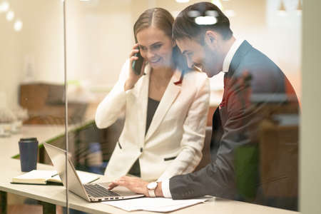 Business partners, stock brokers happy to see their successful buy or sell . Young business people in the suits with looking down at laptop standing behind the glass. Business concept.の写真素材