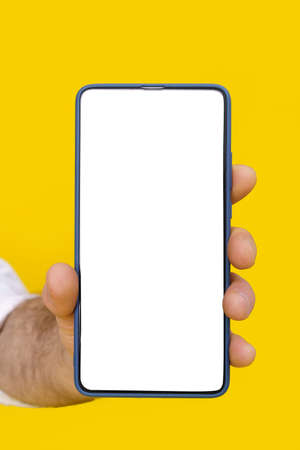 Close up man hand holding smartphone with white blank screen and blue phone case. Isolated on yellow background. Mobile phone frameless design concept for mobile app advertising. Copy space.の写真素材