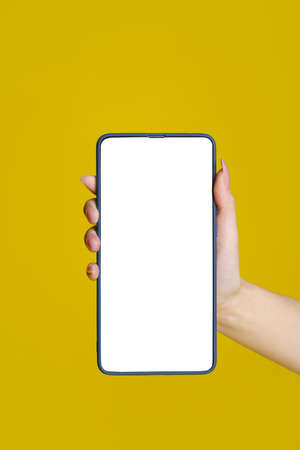 Close up woman hand holding smartphone with green screen and blue phone case. Isolated on yellow background. Mobile phone frameless design concept. Mobile app advertising. Copy space. Great offer.の写真素材