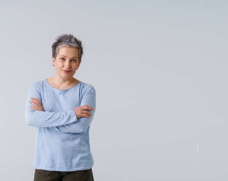 Challenging grey hair mature business woman in 50s posing with hands folded and copy space on right isolated on white background. Copy space and place for product placement. Aged beauty. Toned image.の写真素材