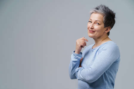 Lovely grey hair mature business woman in 50s posing sideways with hands folded and copy space on right isolated on white background. Copy space and place for product placement. Aged beauty.の写真素材