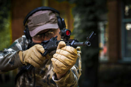 Man with a gun in military uniform tactical hearing protector headset. Police training in shooting gallery with weapon. Civil police man in tactical training course. Selective focus on hand.の写真素材