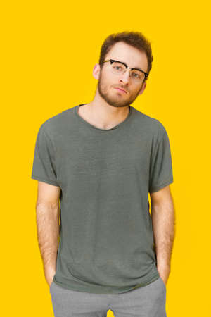 Handsome young man in casual wear and eye glasses posing on yellow background. Stylish bearded smart casual look hipster man. Thoughtful guy on yellow background.の写真素材
