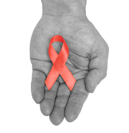 Black and white male hand with red ribbon bow awareness isolated on white background. HIV, AIDS world day. Social life issues concept. Aids charity fund concept. Healthcare and medicine concept.の写真素材