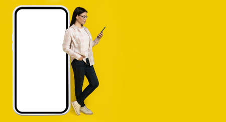 Leaned on big smartphone with white screen charming middle aged asian woman looking at phone in her...
