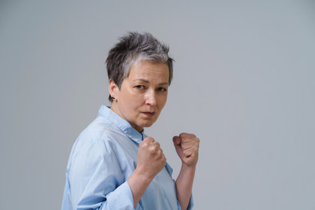 Frightened woman with hands put in fists. Senior woman with grey hair pose as boxing fighter about to stand or protect herself. Human trafficking concept. Confident, strong and aggressive woman.の写真素材