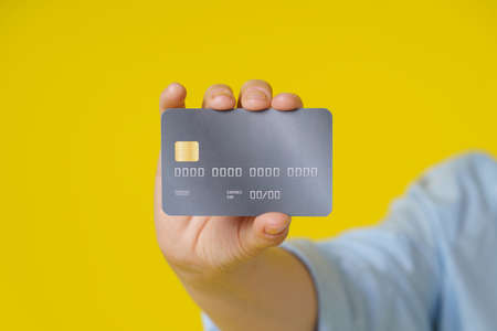 Credit, debit cad close up in hand of mature woman showing it on camera, customer online payment or shopping online, isolated on yellow background. E-commerce, online banking concept.の写真素材