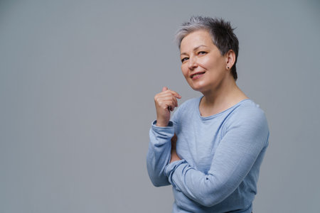 Mature woman 50s with grey hair posing with hands folded and copy space on left isolated on white background. Copy space and place for product placement. Mature people healthcare concept.の写真素材