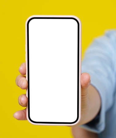 Woman hand holding smartphone with white screen in pink case isolated on yellow background. Modern...
