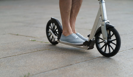 Man feet on scooter close up wearing in a sneakers shoes. Scooter with big wheels man having a ride on the streets or park after work outdoors. No face visible. Selective focus on feet.の写真素材