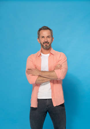 Strong handsome middle aged man with grey beard 40s, 50s wearing casual isolated on blue background. Smiling mature muscular, fit, athletic man posing in studio. Mature fit man health and physics.の写真素材