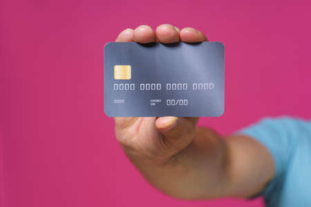 Dark grey-purple debit, credit card in man hand isolated on pink background. Financial, banking concept. No face visible.の写真素材