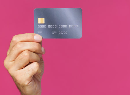 Great offer. Dark grey-purple debit, credit card in man hand isolated on pink background. Financial, banking concept. No face visible.の写真素材