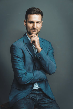 Elegance Businessman in a Blue Formal Waist Up Suit Jacket Gazes Straight to the Camera. Elegant Brown Haired Man Posing in Studio on a Gray Background. . High quality photoの写真素材