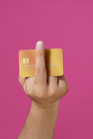 Aggressive hand gesture fuck you male hand holding debit, credit card between fingers isolated on pink background. Banking, finances concept. Male hand with bank card.の写真素材