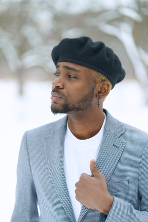 Young man in beret like Che Guevara stay on winter background. African american hold jacket looking aside. High quality photoの写真素材