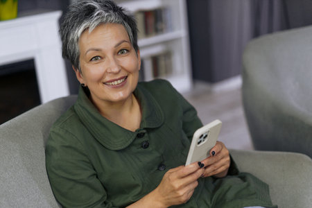 Happy woman is smiles brightly indoors. Surrounded by the warmth of her home, she exudes sense of contentment and peace. Her smile is contagious, spreading positivity. High quality photo.の写真素材
