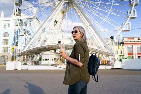 Stylish and confident mature woman with grey hair enjoys refreshing juice cup in vibrant European city, exuding elegance and positivity. The image captures the joy and active lifestyle of mature woman who is still fashion-savvy and full of life. High quality photoの写真素材